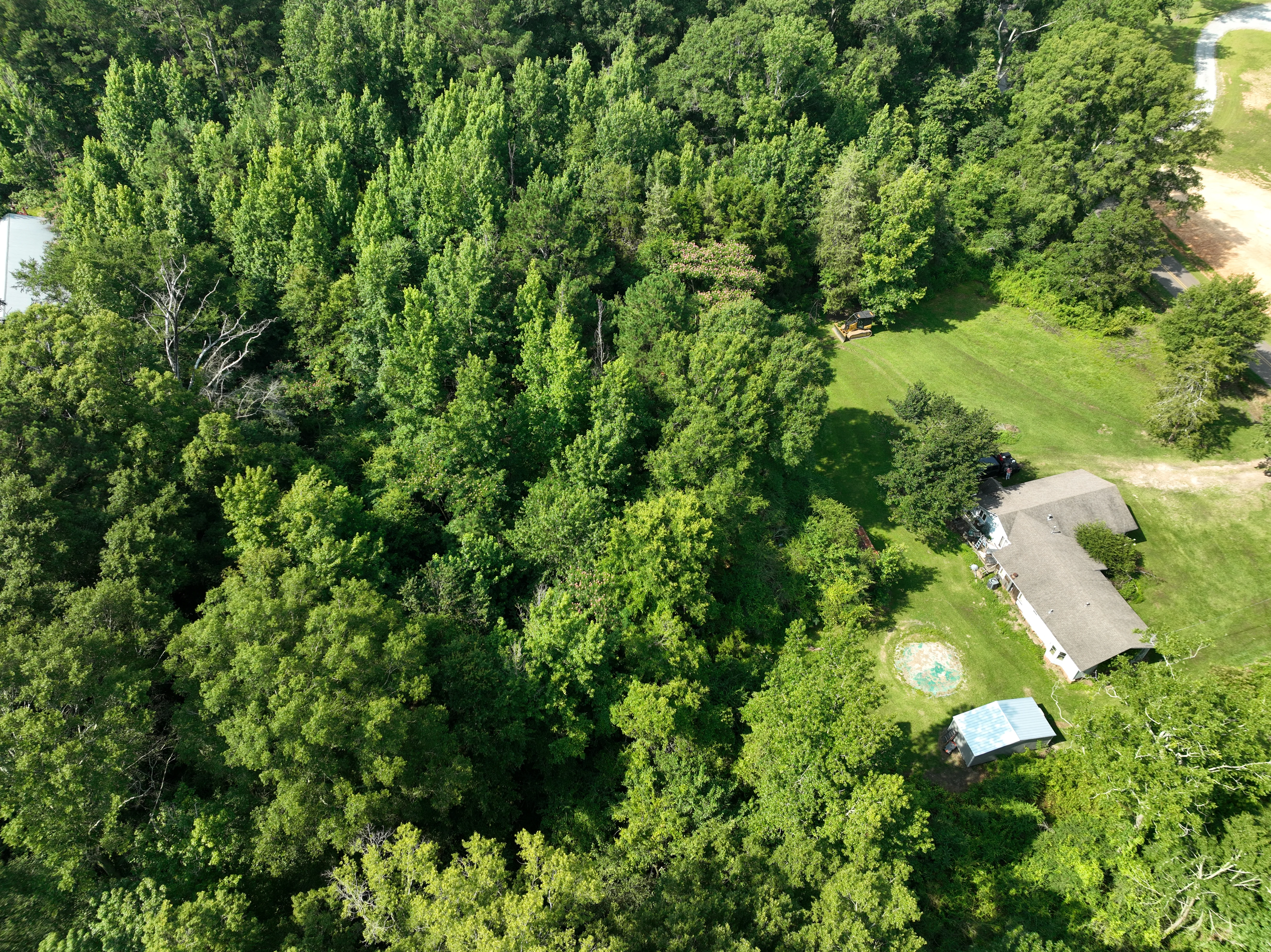 Aerial view of cleared residential lot with house foundation, surrounded by dense forest and green lawn