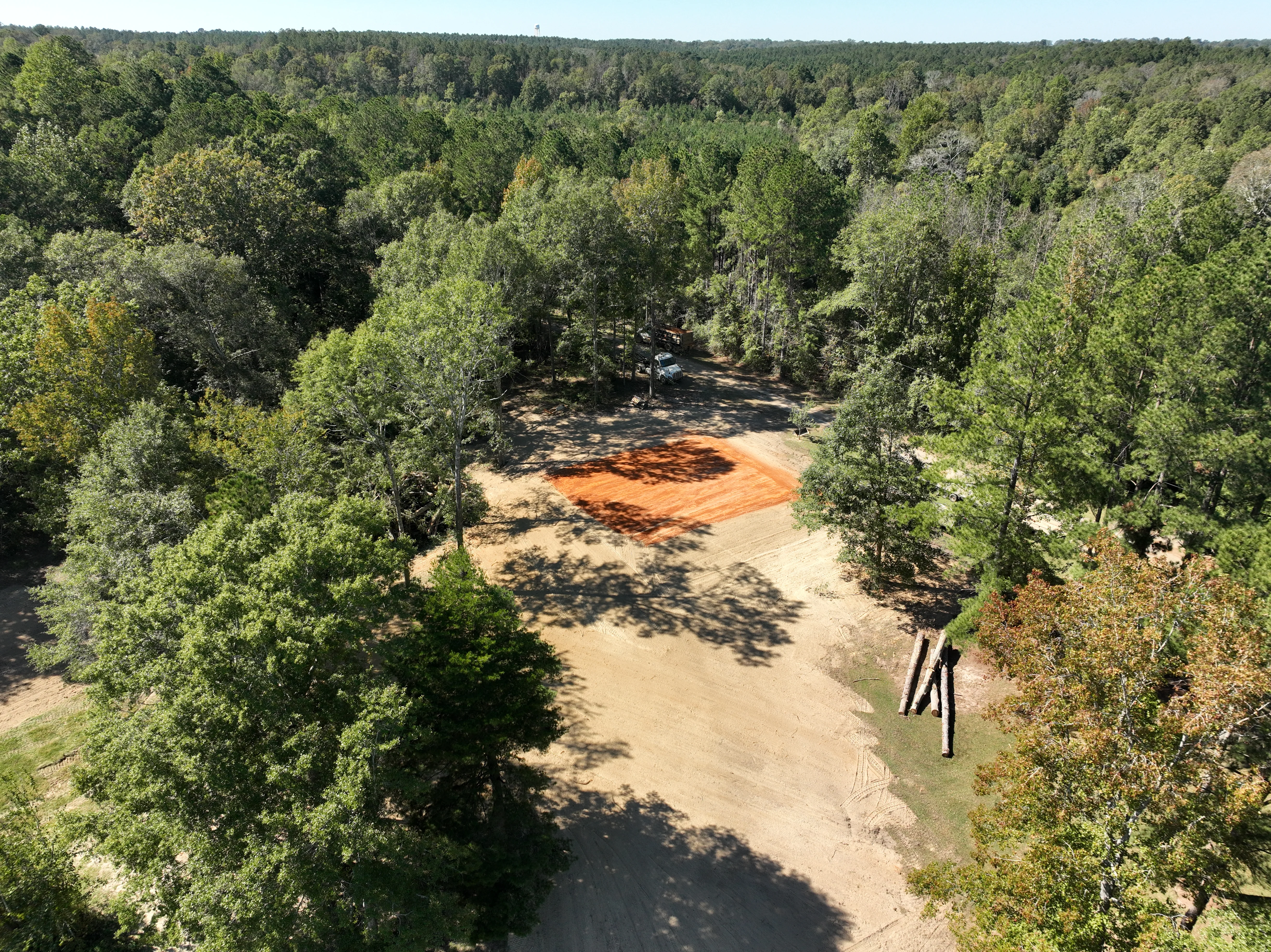 Aerial view of cleared forest land with red clay excavation area surrounded by mature trees