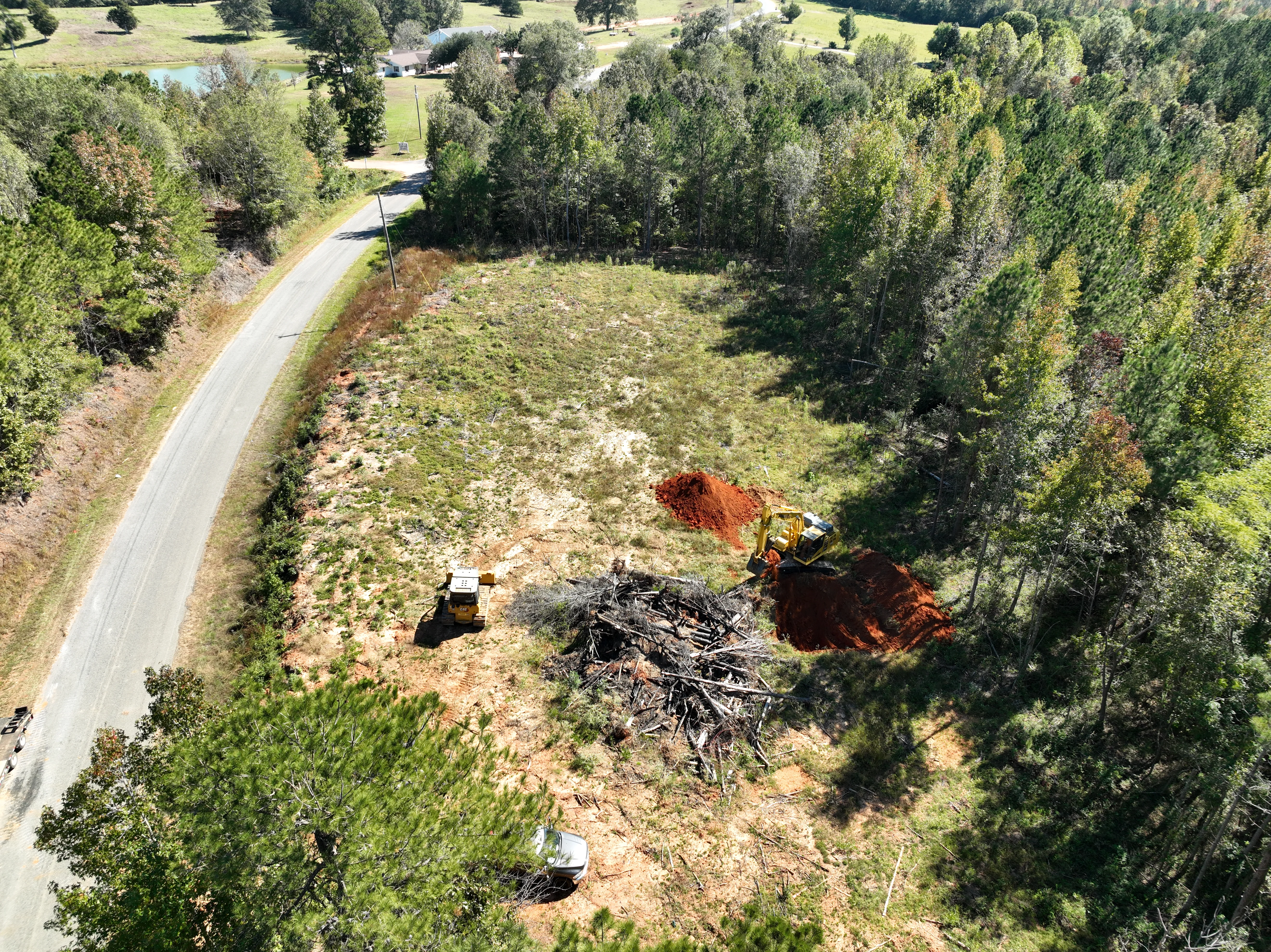 Aerial view of excavation site with dozers clearing timber and moving red clay material on wooded property