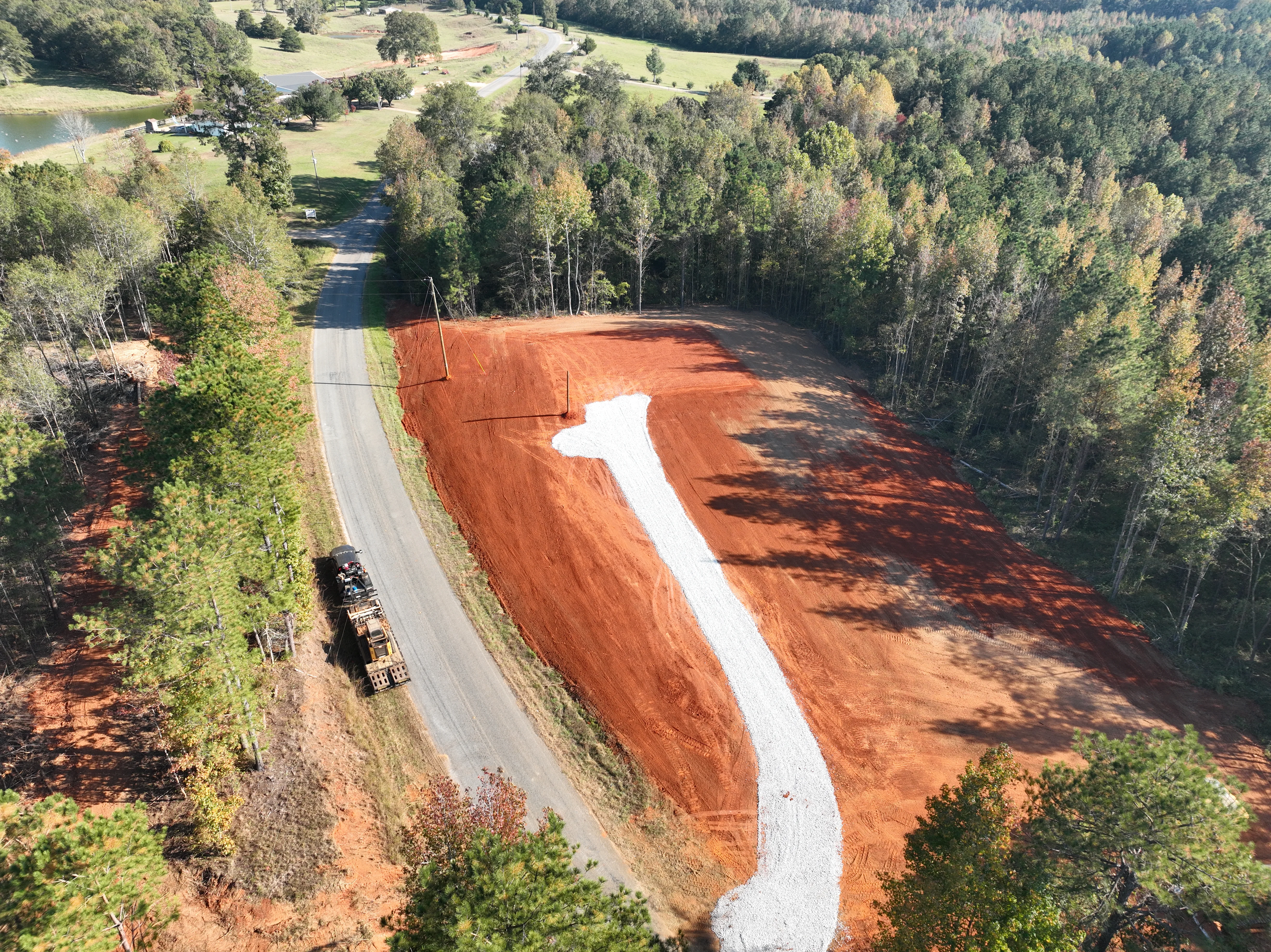 Aerial view of cleared land with white drainage swale through red clay excavation site surrounded by forest